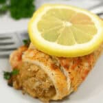 A close-up of a seasoned fish fillet with crabmeat stuffing, garnished with a lemon slice and parsley on a white plate.