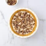 A Chocolate and Peanut Butter Pie topped with chopped chocolate and peanut butter candies sits on a marble surface next to a small bowl of additional chopped candies.