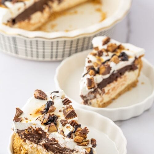 Two slices of Chocolate and Peanut Butter Pie with whipped topping and chopped peanut butter cups are served on small plates, while the remaining pie rests in a ceramic dish in the background.