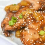 Close-up of grilled fish fillets glazed with teriyaki sauce, garnished with pineapple chunks, green onions, and sesame seeds, served on a white plate. For a delightful twist, imagine this presentation with the tender flavors of slow cooker honey garlic chicken.