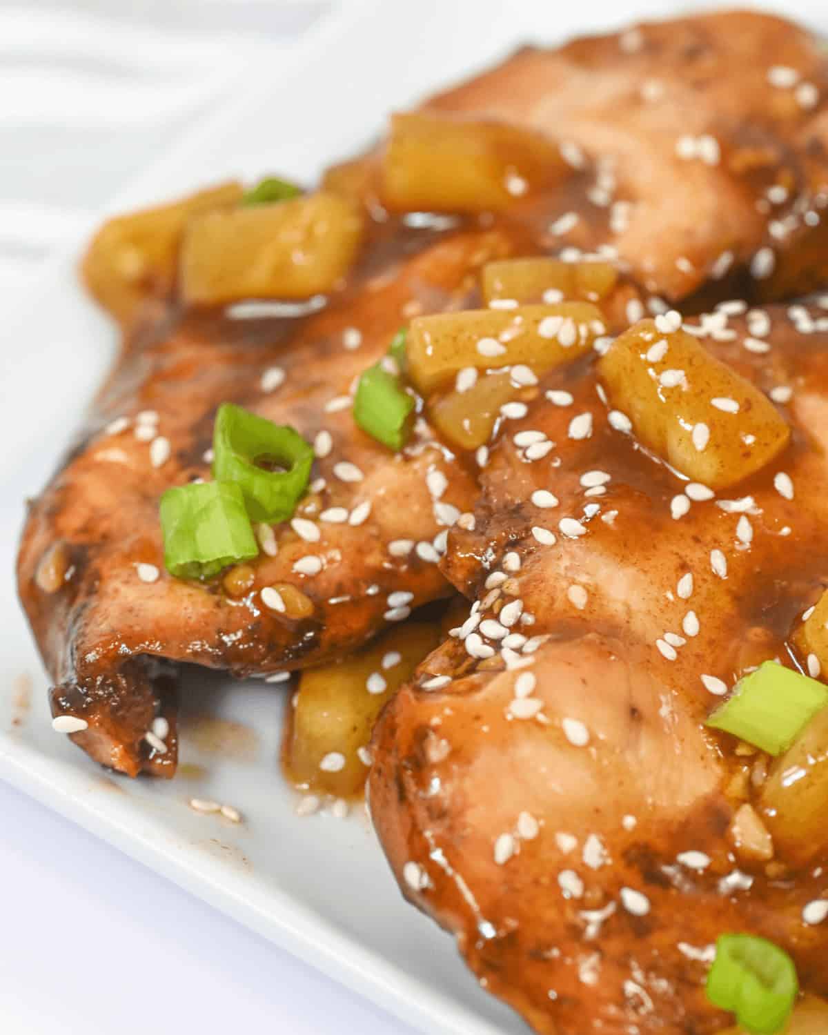 Close-up of grilled fish fillets glazed with teriyaki sauce, garnished with pineapple chunks, green onions, and sesame seeds, served on a white plate. For a delightful twist, imagine this presentation with the tender flavors of slow cooker honey garlic chicken.
