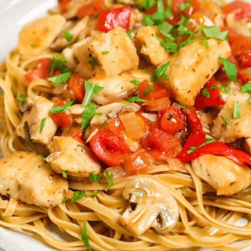 A plate of pasta topped with easy chicken cacciatore featuring diced chicken, chopped tomatoes, and mushrooms, all garnished with fresh herbs.