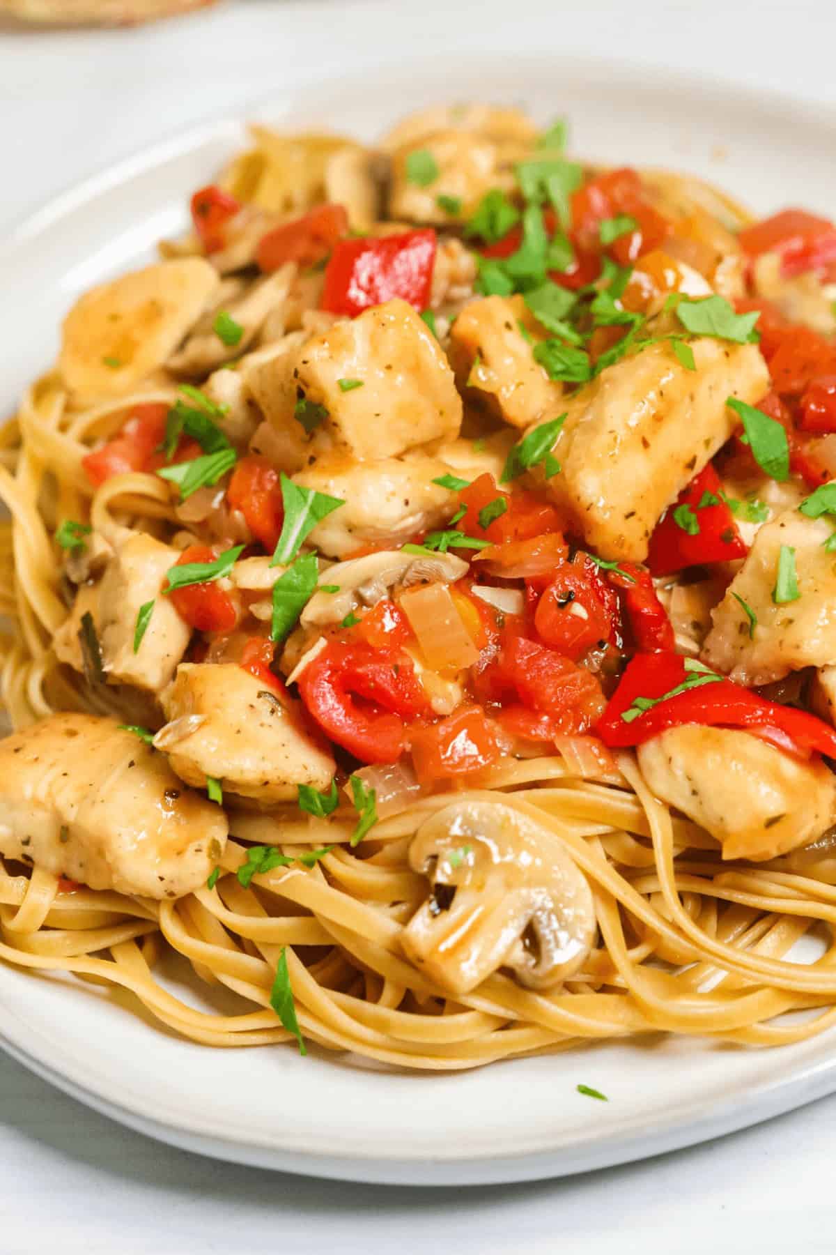 A plate of pasta topped with easy chicken cacciatore featuring diced chicken, chopped tomatoes, and mushrooms, all garnished with fresh herbs.
