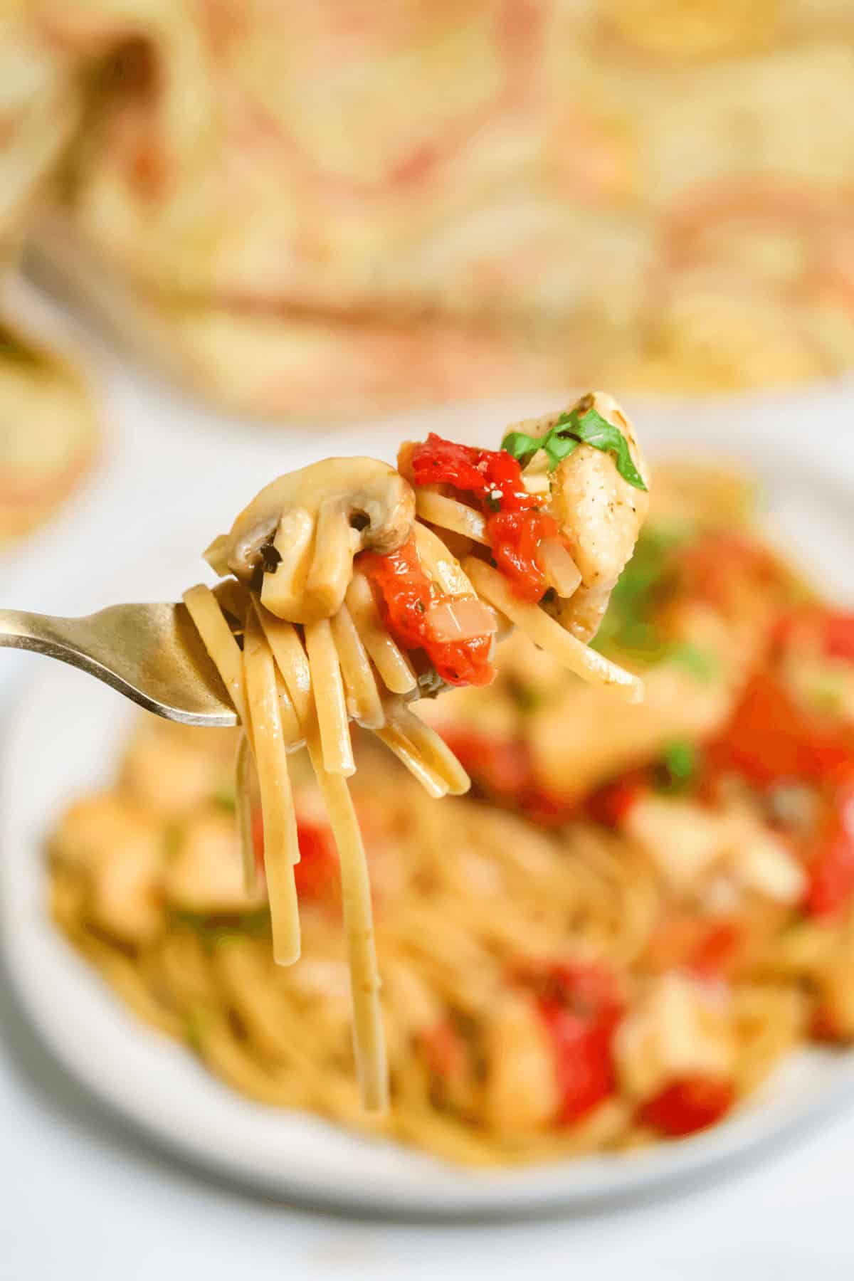 A fork with pasta, mushrooms, and diced red bell peppers hovers above a plate, reminiscent of an easy chicken cacciatore feast.
