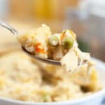 A spoon is being held up to a bowl of chicken cobbler.