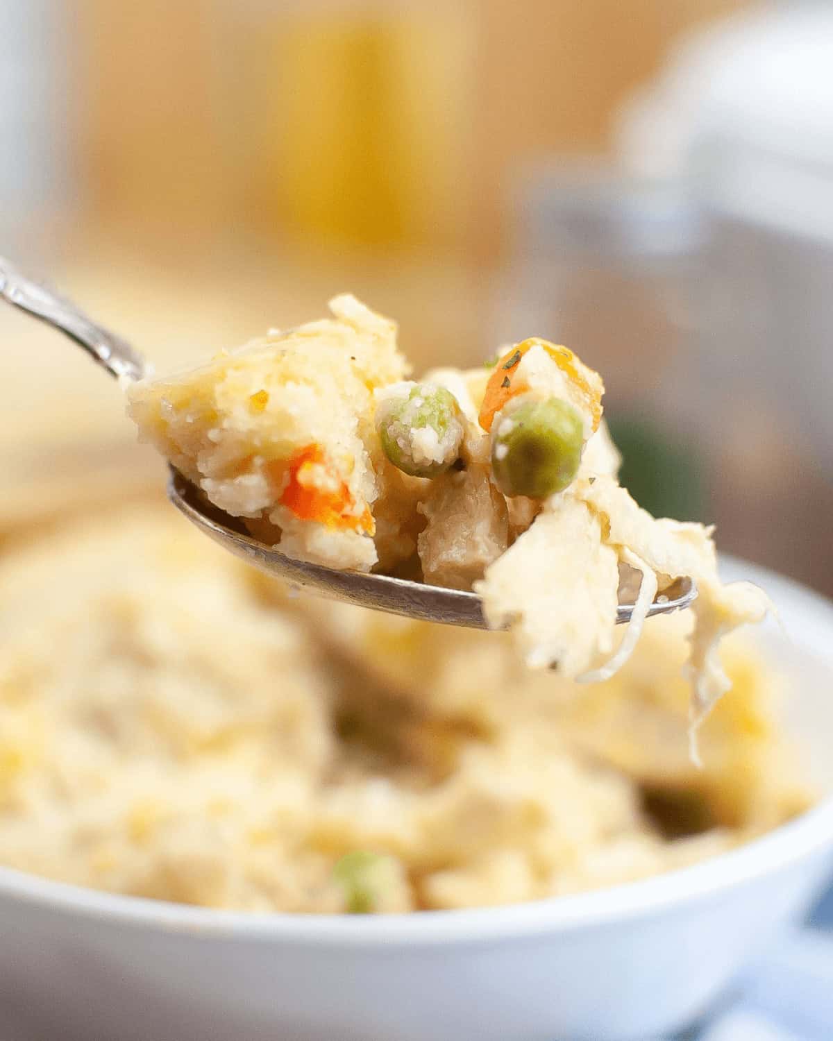 A spoon is being held up to a bowl of chicken cobbler.