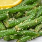 A white plate with garlic parmesan green beans and lemon slices.