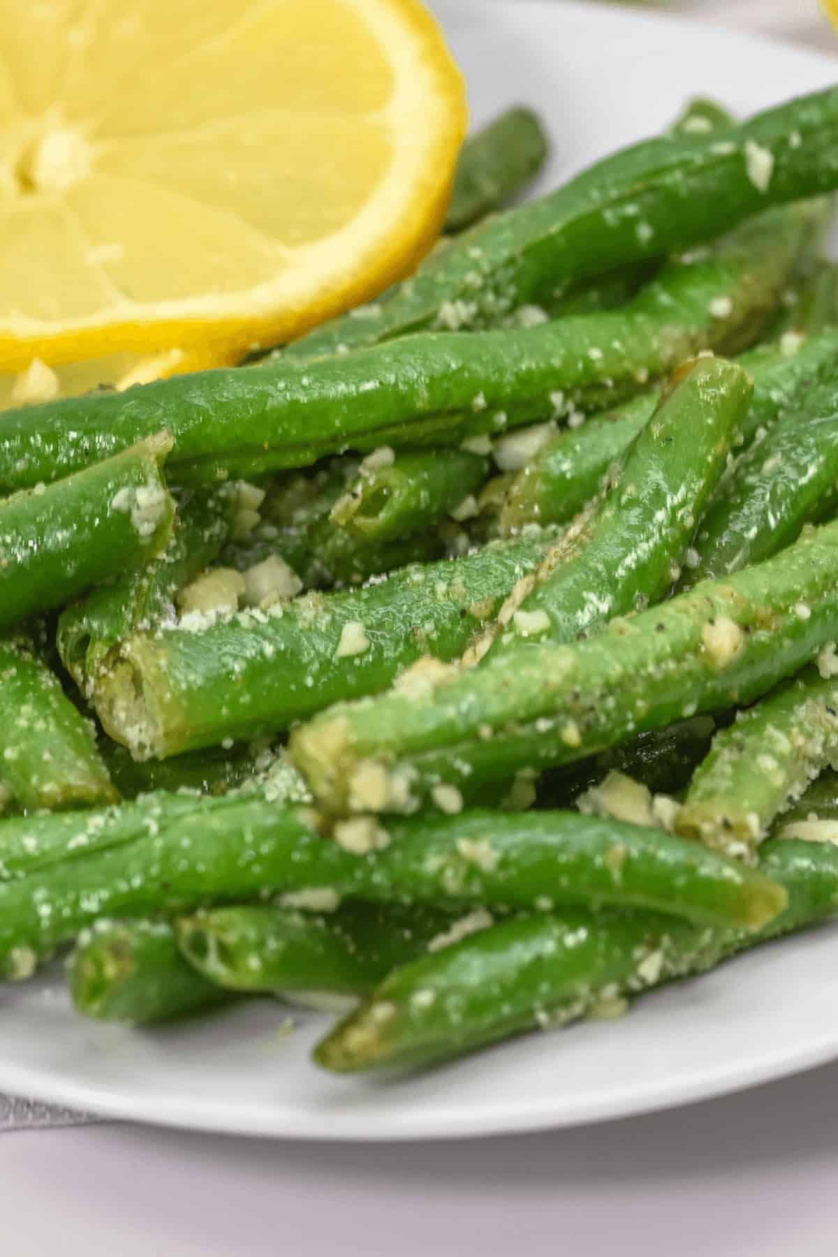 A white plate with garlic parmesan green beans and lemon slices.