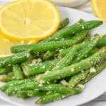 A plate of garlic Parmesan green beans is elegantly garnished with lemon slices, while a bowl of grated cheese sits invitingly in the background.