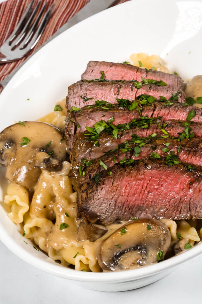 Filet Mignon in Sherry Mushroom Cream Sauce in a white bowl with a fork