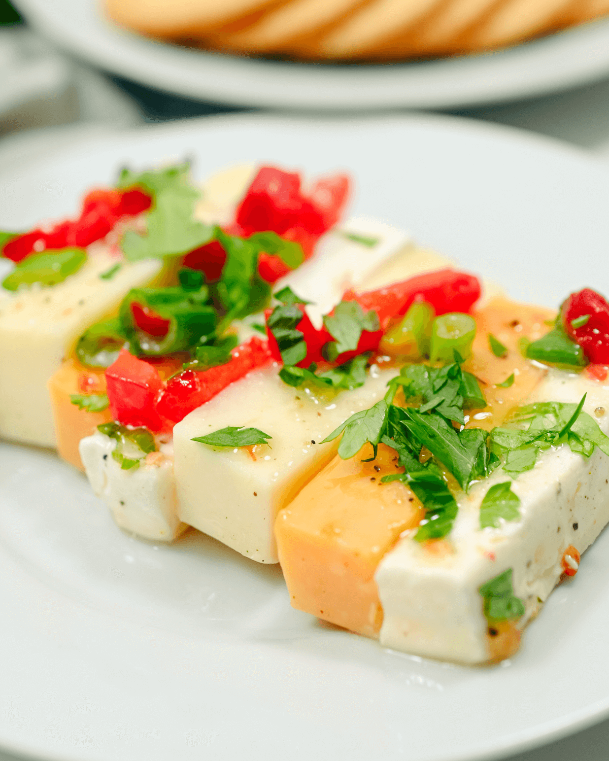 A plate of marinated cheese and vegetables on a white plate.