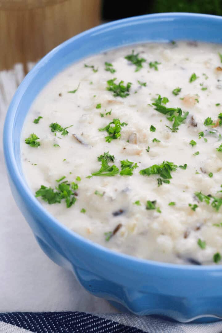 A blue bowl filled with creamy chicken and rice soup, garnished with chopped parsley.
