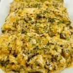 A white plate with pan seared pork chops covered in sauce and herbs.