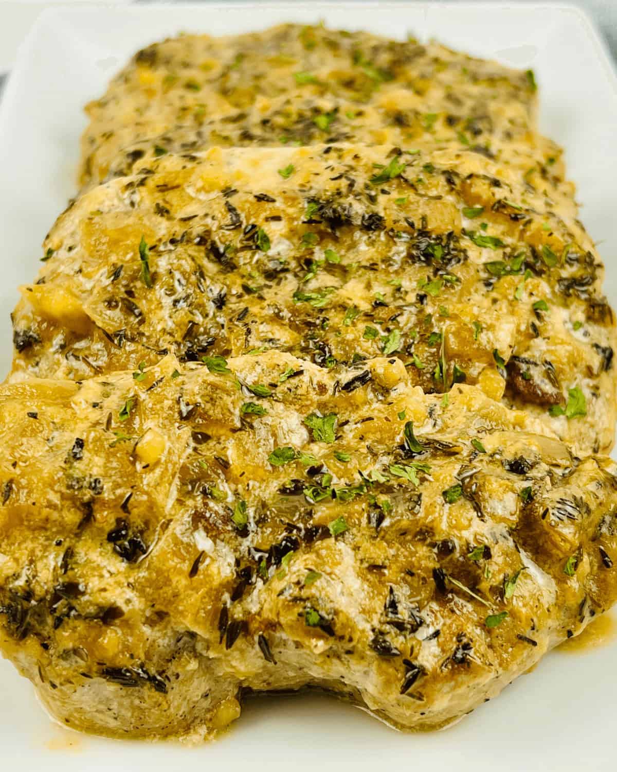 A white plate with pan seared pork chops covered in sauce and herbs.