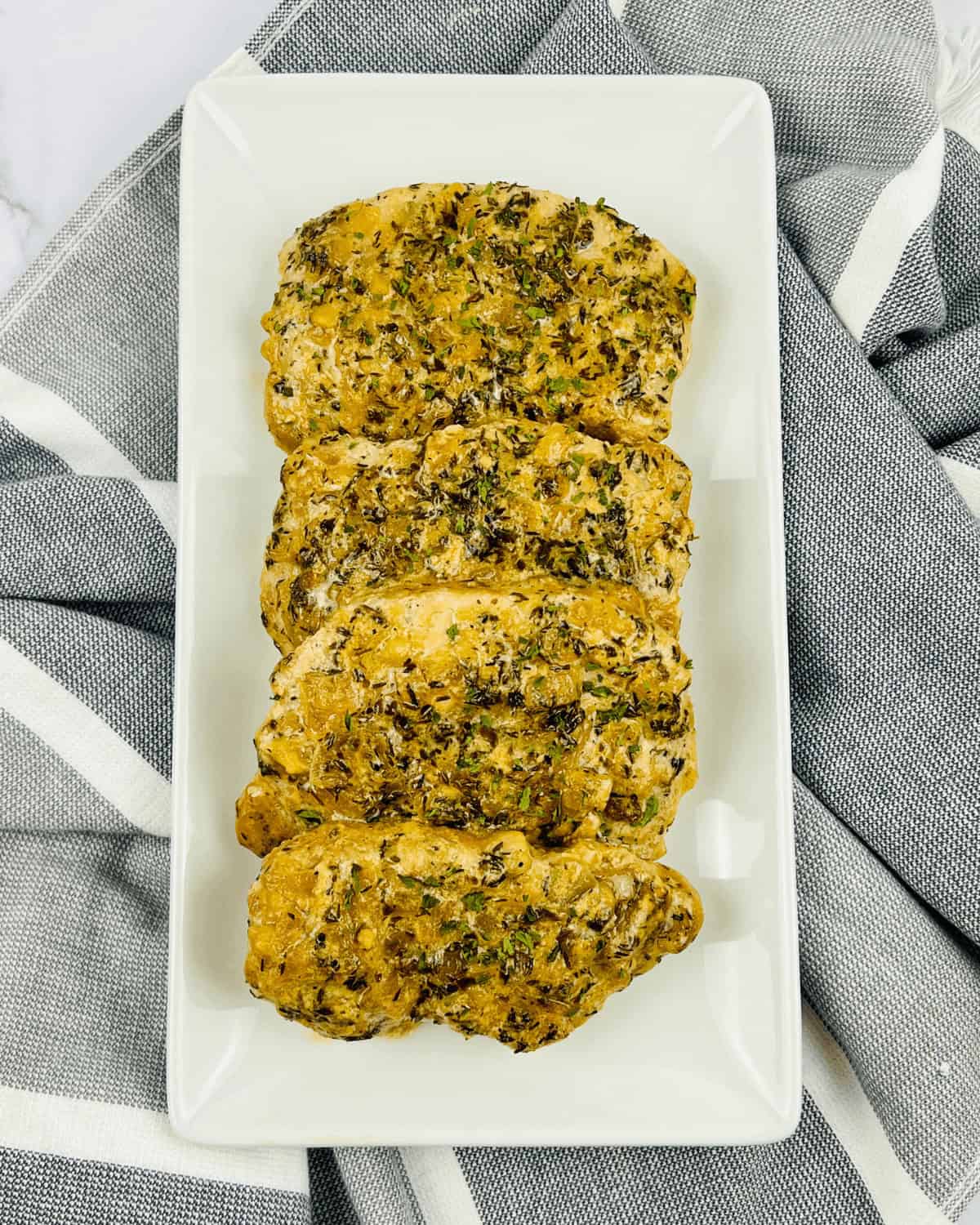 Creamy Pan seared pork chops with herbs on a white plate.