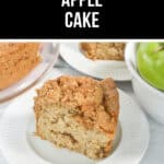 A slice of fresh apple cake rests on a white plate, beside a whole cake and a bowl of green apples.
