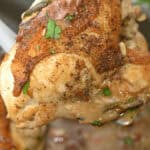 A cooked piece of Herbed Lemon Chicken with a crispy skin is held up with tongs, showcasing the perfect blend of herbs and zesty lemon sauce.