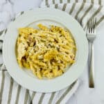 A plate of creamy chicken cordon bleu casserole with herbs on a striped cloth with a fork on the side.