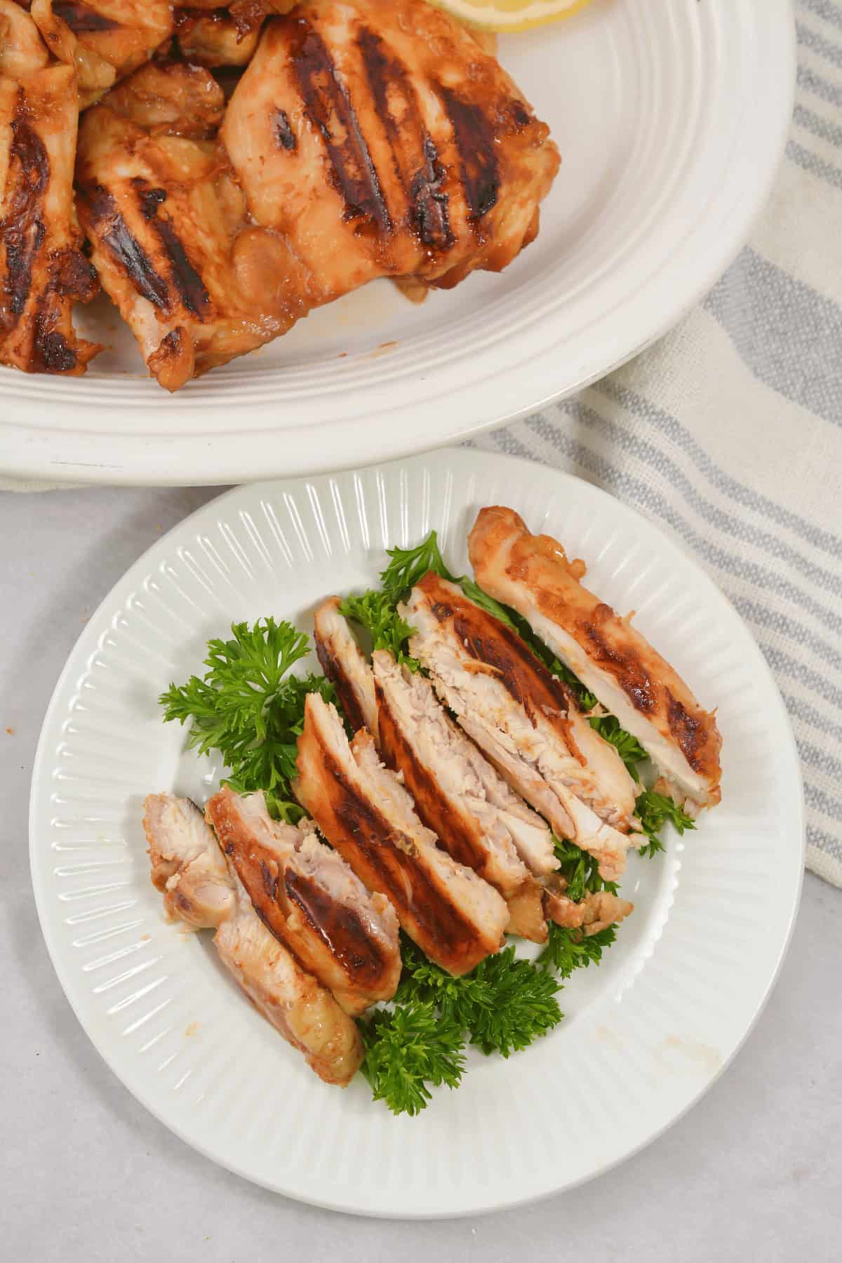 Strips of the Asian grille chicken on a platter surrounded by parsley.