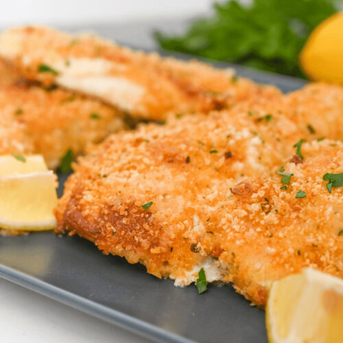 Parmesan herb crusted fish fillets on a plate with lemons and parsley.