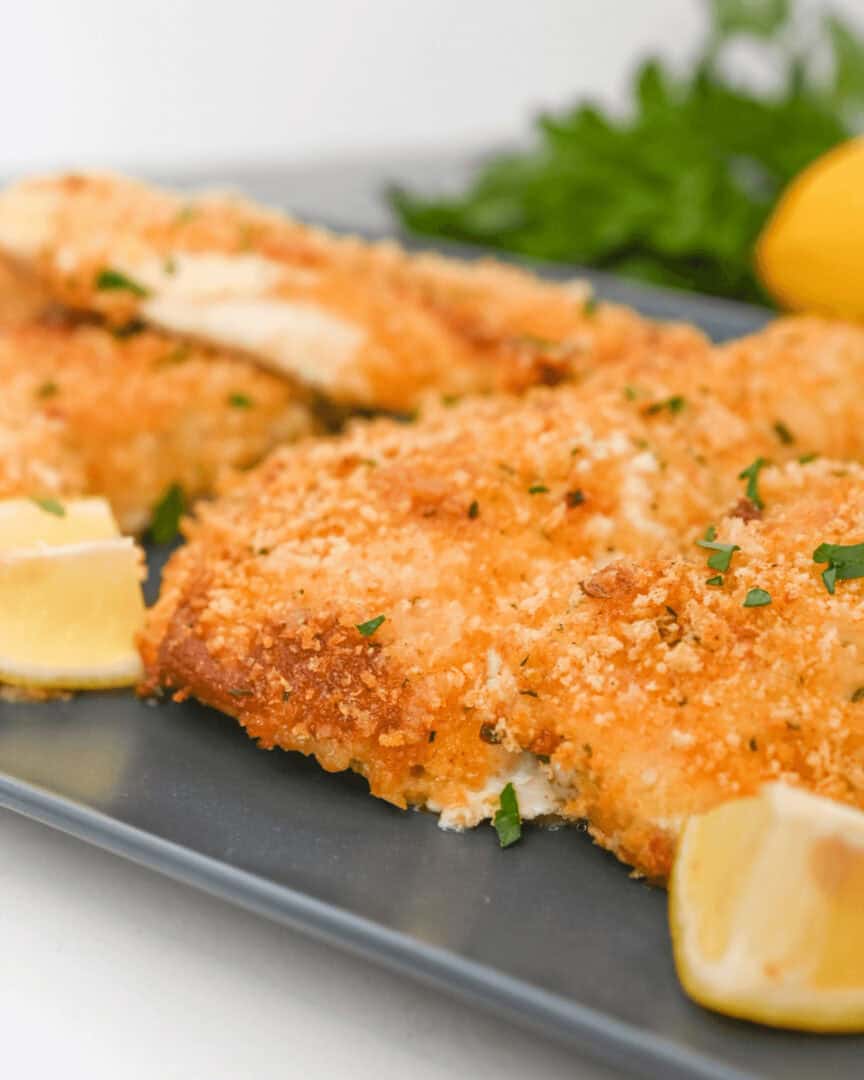 Parmesan herb crusted fish fillets on a plate with lemons and parsley.