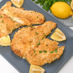 Parmesan herb crusted chicken with lemon and parsley on a plate.