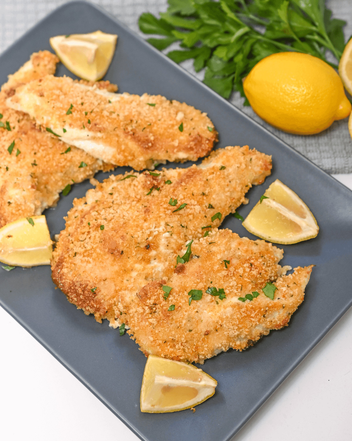 Parmesan Herb Crusted Chicken with lemon and parsley on a plate.