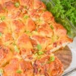 A glass baking dish filled with golden-brown Biscuit Breakfast Casserole rolls, topped with chopped green herbs, sits next to a bunch of fresh parsley.