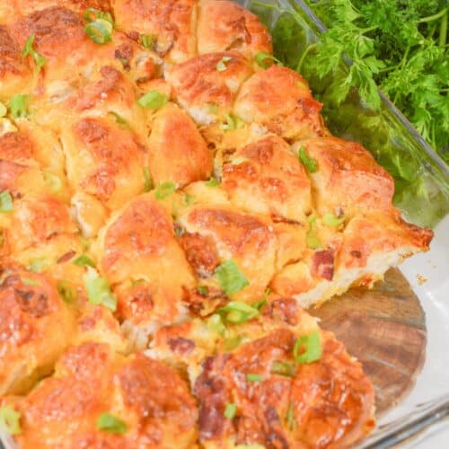 A glass baking dish filled with golden-brown Biscuit Breakfast Casserole rolls, topped with chopped green herbs, sits next to a bunch of fresh parsley.