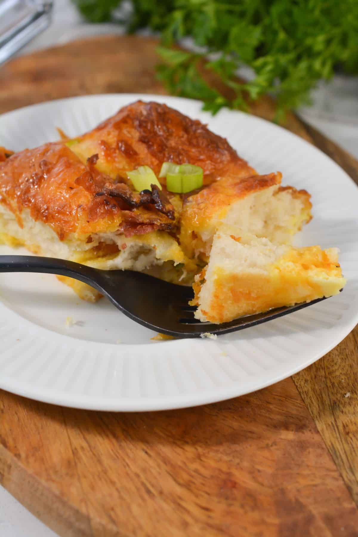 A slice topped with green onions sits on a white plate, with a fork holding a bite-sized piece.