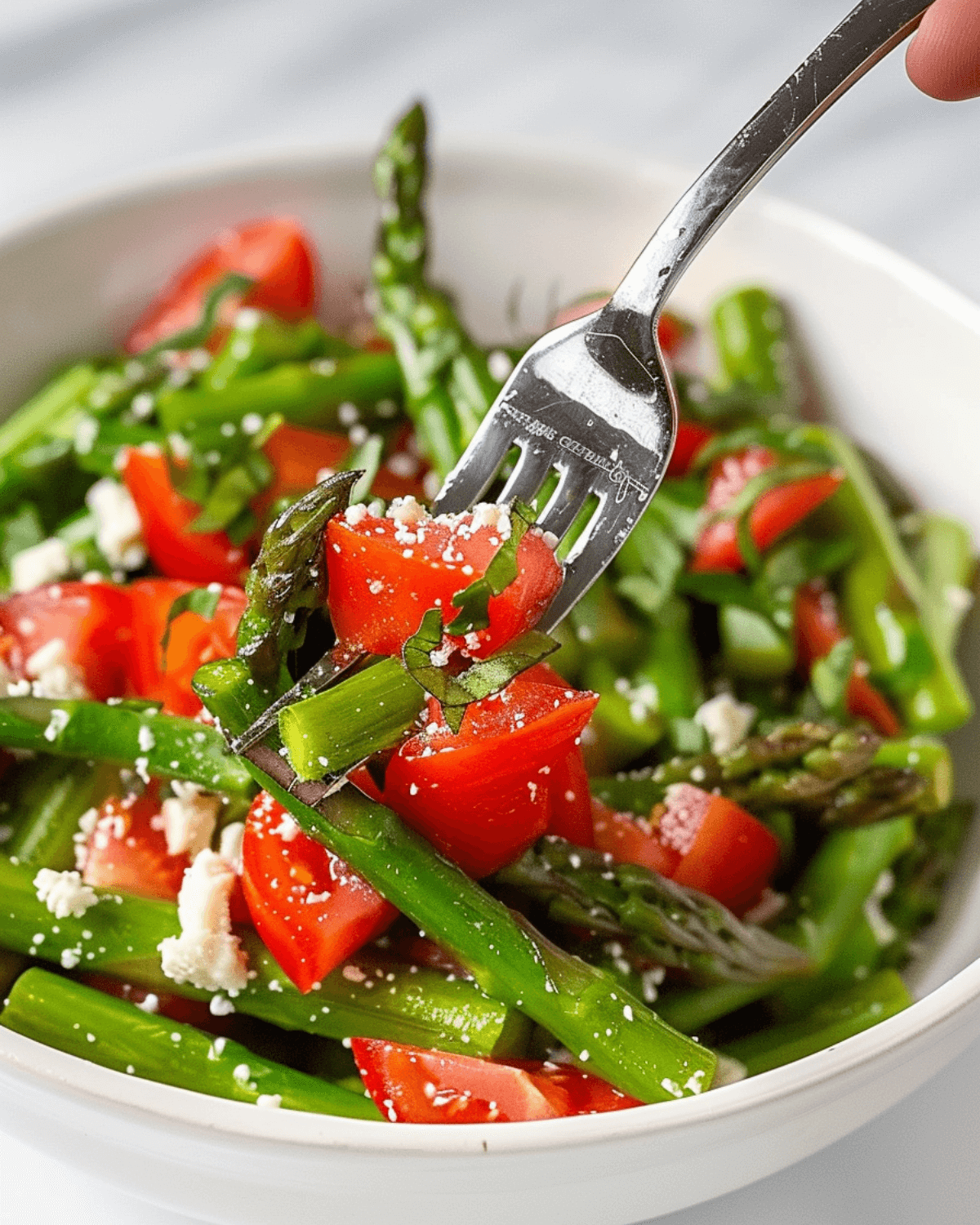 A bowl of fresh side dish topped with crumbled cheese, with a fork picking up some asparagus.