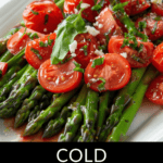 A vibrant dish of tomato and asparagus salad topped with halved cherry tomatoes, crumbled cheese, and fresh herbs, served on a white rectangular plate.