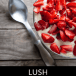 A bowl of lush strawberry angel food cake dessert sits enticingly next to a spoon on a wooden surface.