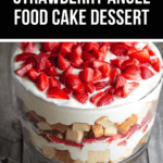         A layered strawberry angel food cake dessert in a glass trifle dish, featuring cubed cake, creamy filling, and fresh strawberry slices on top. The caption above captures the essence of this delightful treat.