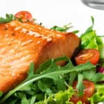 Grilled Salmon Salad features perfectly grilled salmon on a bed of mixed greens, complemented by cherry tomatoes and crisp cucumber slices.