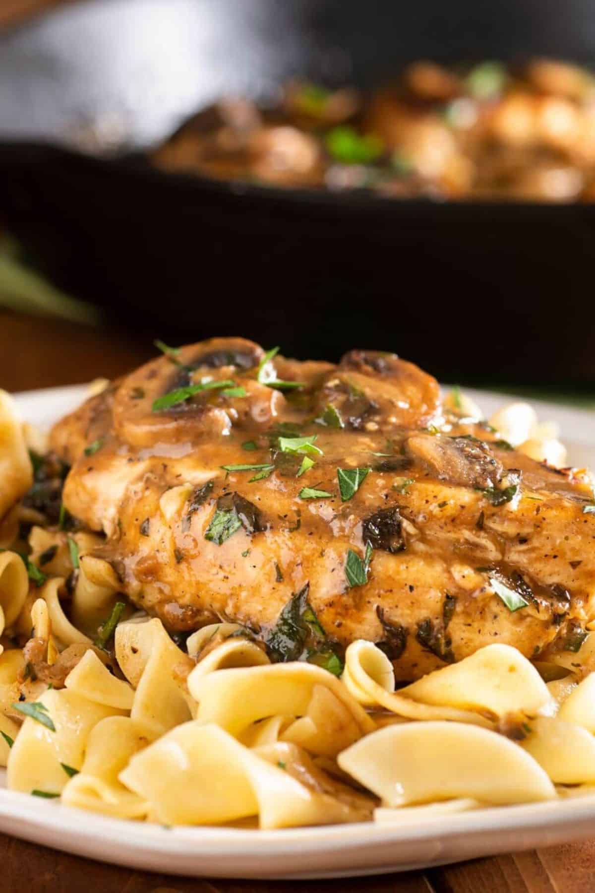 The finished dish with mushrooms, sauce and  with chopped parsley, with a skillet in the background.