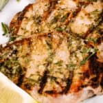 Grilled Boneless Pork Chops garnished with herbs and a lemon wedge on the side.