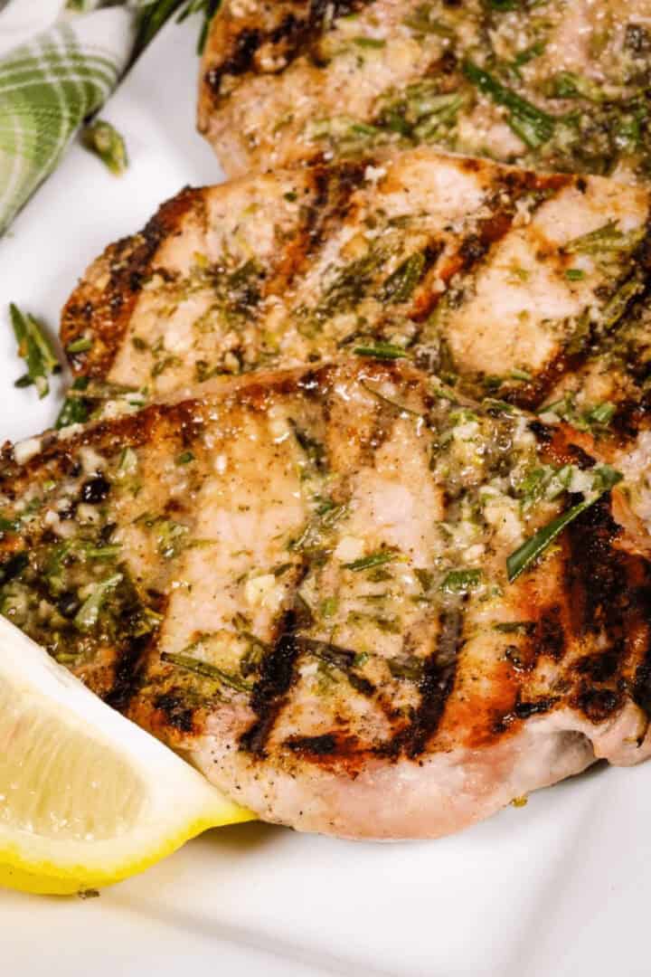 Grilled Boneless Pork Chops garnished with herbs and a lemon wedge on the side.