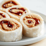 A plate of Peanut Butter and Jelly Pinwheel Sandwiches (PBJ Sushi) on a table.