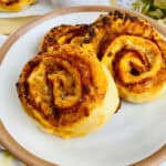 Three treats on a plate with a side of marinara sauce in bowls, set on a wooden serving board.