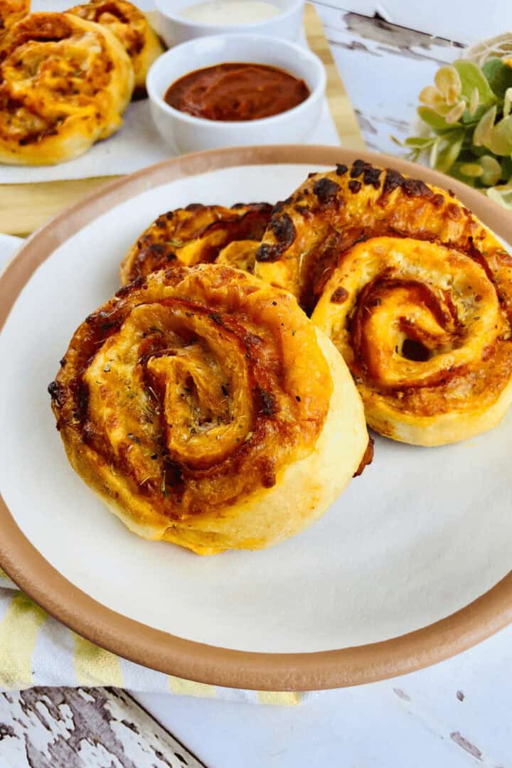 Three treats on a plate with a side of marinara sauce in bowls, set on a wooden serving board.