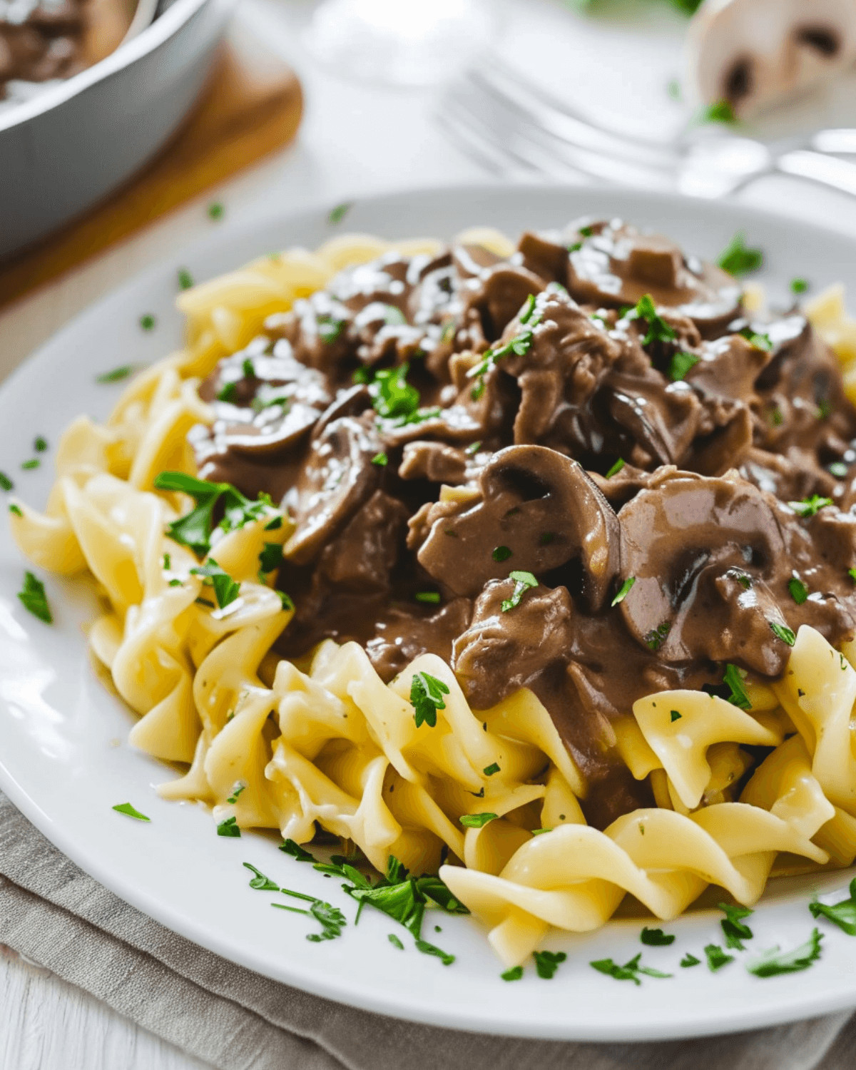 A plate of venison stroganoff with pasta on a wooden table.