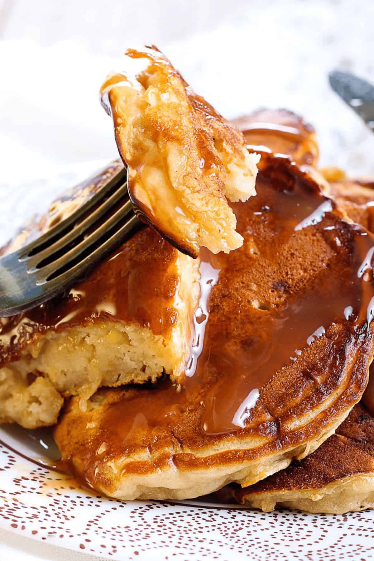Close-up of fluffy breakfast topped with syrup, partially cut with a fork on a white patterned plate.