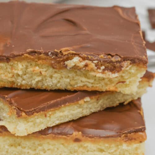 Three square pieces of chocolate and peanut butter cake-topped shortbread stacked on a white plate.