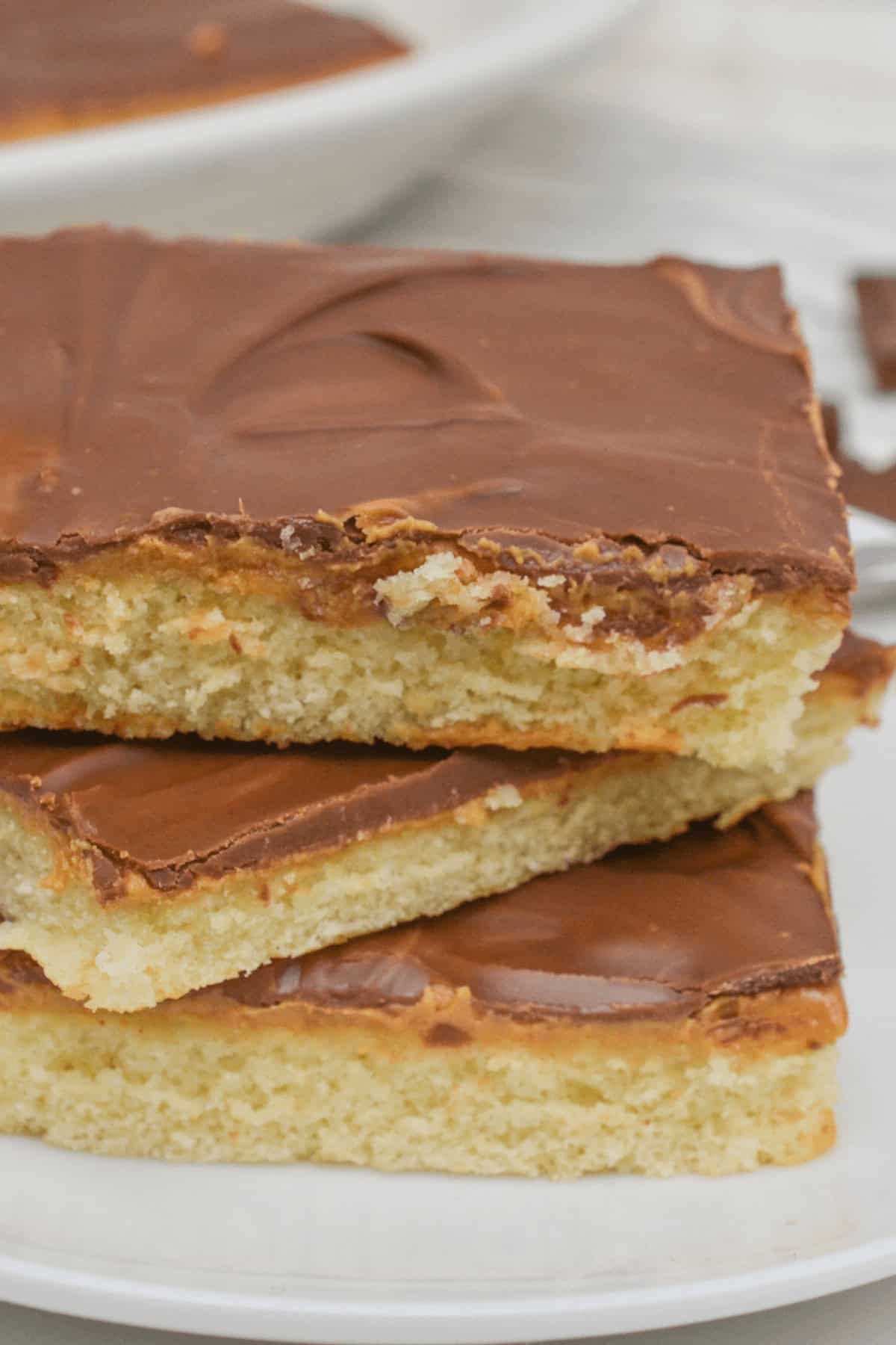 Three square pieces of chocolate and peanut butter cake-topped shortbread stacked on a white plate.