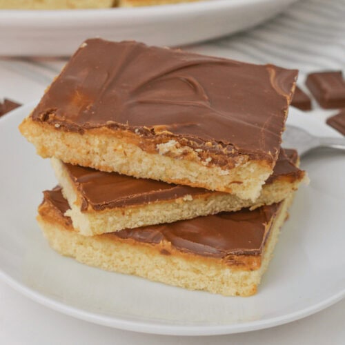 Three square slices of chocolate and peanut butter cake with rich, velvety frosting are elegantly stacked on a pristine white plate.