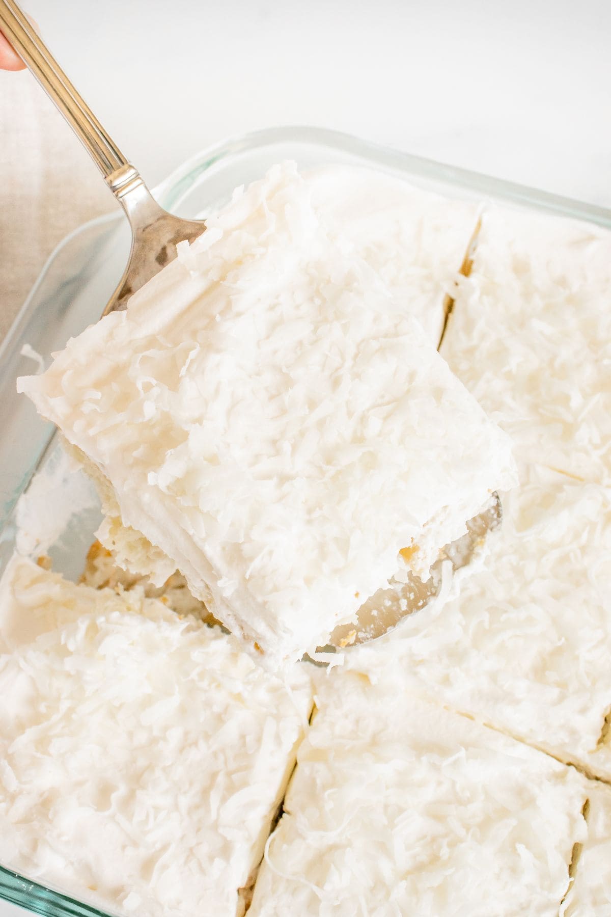 A square topped with shredded coconut, is being lifted from a glass baking dish filled with several other delicious cut pieces.