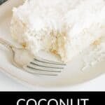 A slice of Coconut Poke Cake with white frosting and shredded coconut sits on a plate next to a fork.