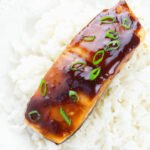 A piece of maple glazed salmon on a bed of white rice garnished with green onions.