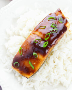 A piece of maple glazed salmon on a bed of white rice garnished with green onions.